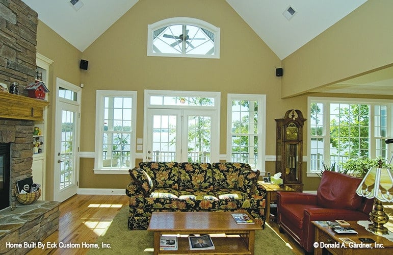 Living room with floral sectional sofa, red leather armchair, stone fireplace, and a french door that leads out to the deck.