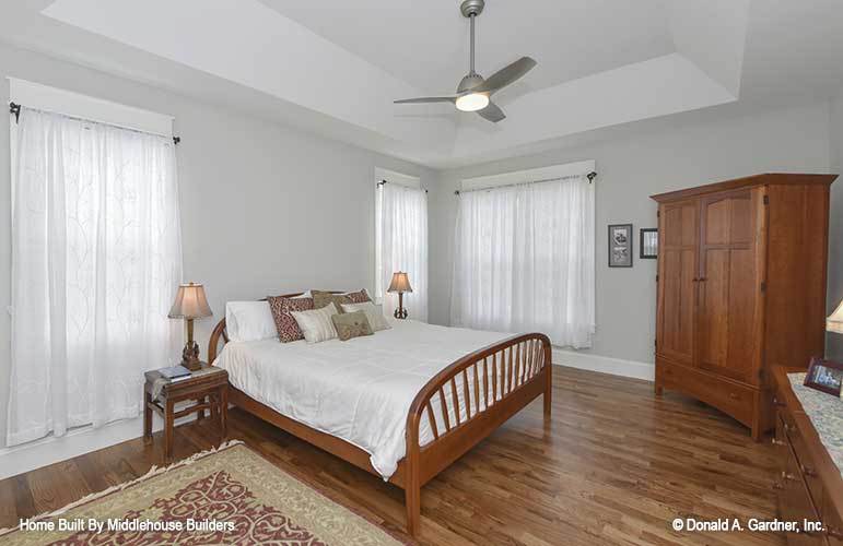 Primary bedroom with a tray ceiling and hardwood flooring that's topped with a tasseled area rug.