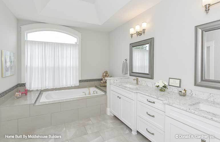 The primary bathroom has a deep soaking tub and a dual sink vanity paired with silver framed mirrors.
