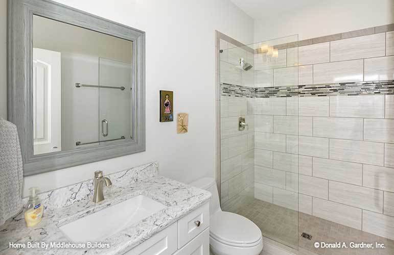 Bathroom with a walk-in shower, a toilet, and a sink vanity crowned with white marble countertop.