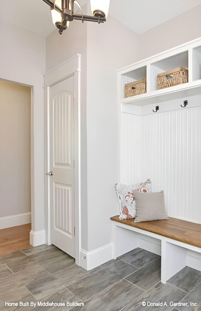 Mudroom with wide plank flooring and white beadboard wall fixed with built-in storage and seat.