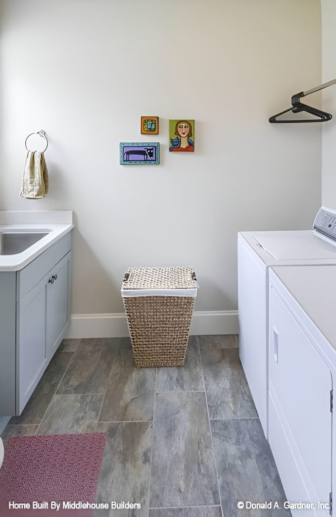 Utility room with white appliances, a rattan hamper, and an undermount sink fitted on the marble top counter.