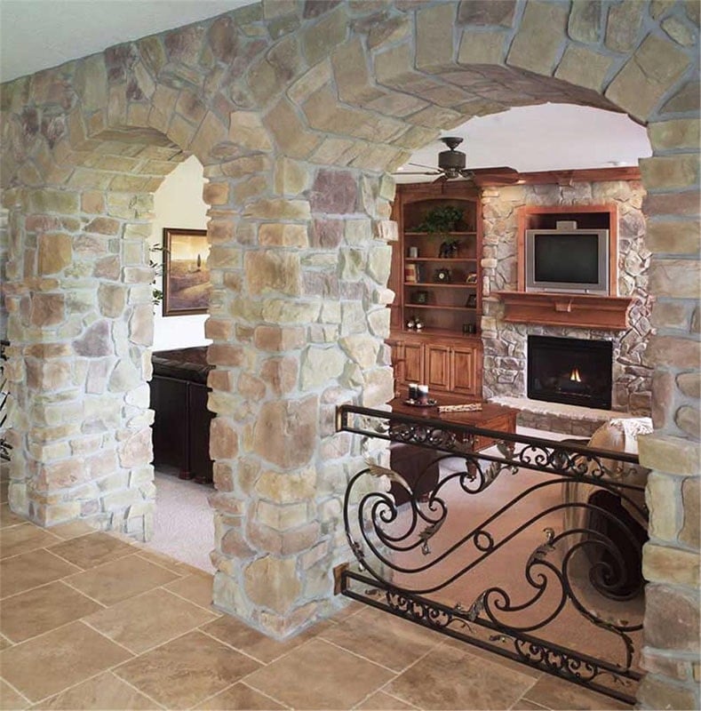 An arched hallway adorned with intricate railings and large stones leads to the cozy living room.