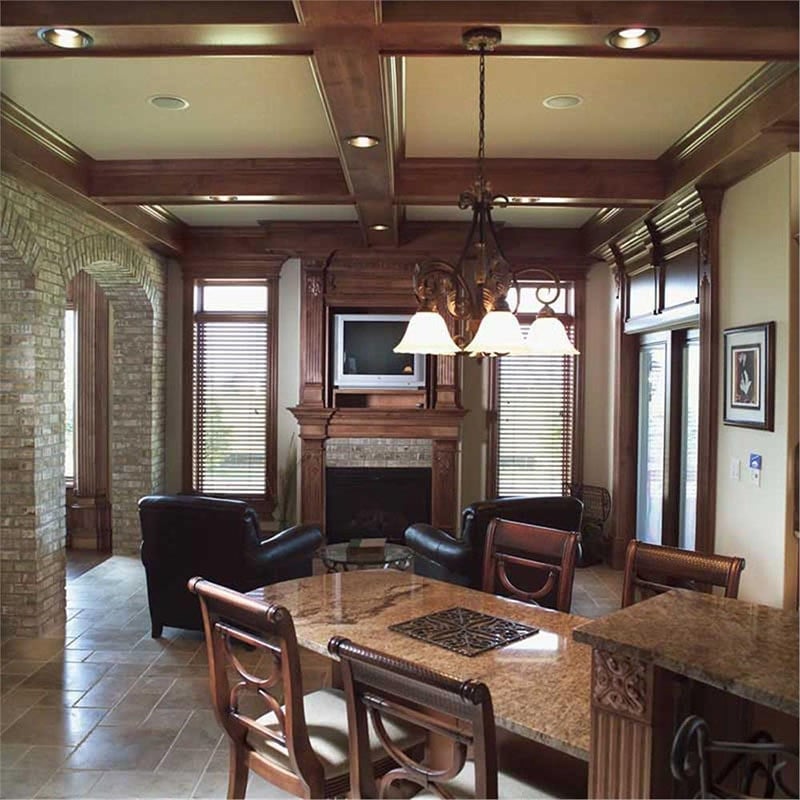Keeping room with a wooden coffered ceiling, black leather armchairs, and a fireplace topped with a small TV.