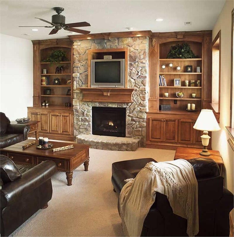 The family room has wooden tables, black leather seats, and a stone fireplace nestled in between the built-in shelves and base cabinets.