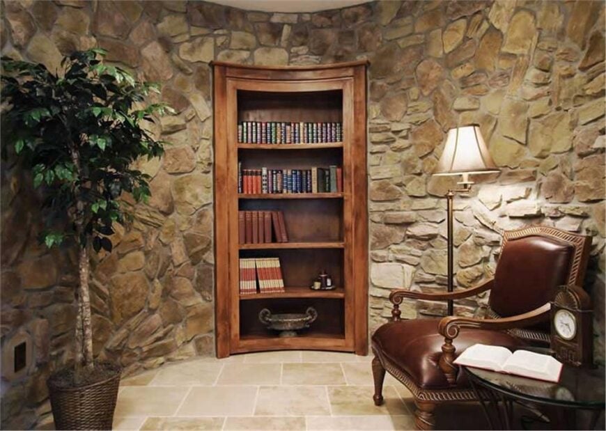 Quiet den with a round side table, a brown leather armchair, and an inset bookcase fitted on the curve stone wall.