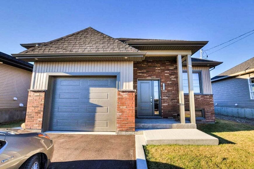 Home's front view showing the vertical exterior siding, brick accents, hipped roofs, and a front-load garage.