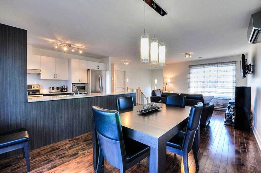 The dining area offers black leather chairs and a rectangular dining table illuminated with cylindrical pendants.