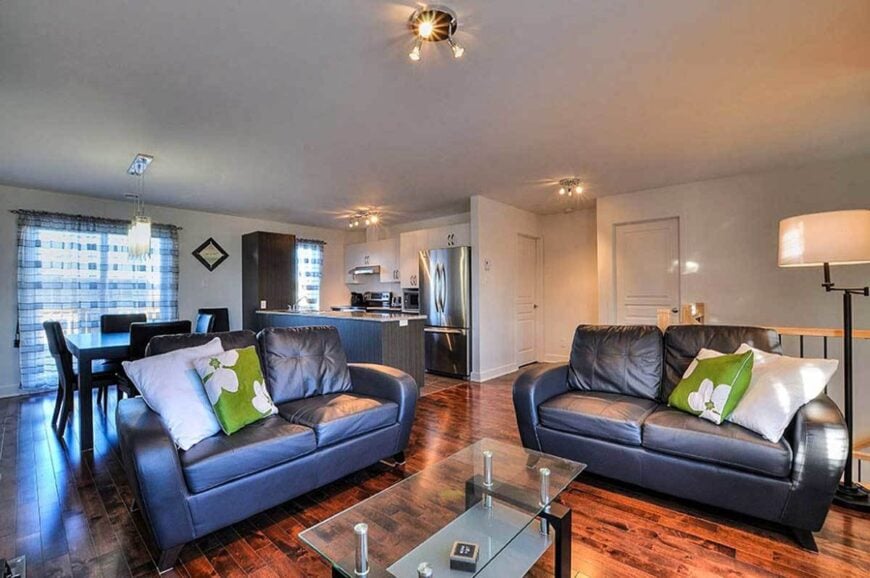 Living room with a glass top coffee table and sectional loveseats accented with white and green floral pillows.