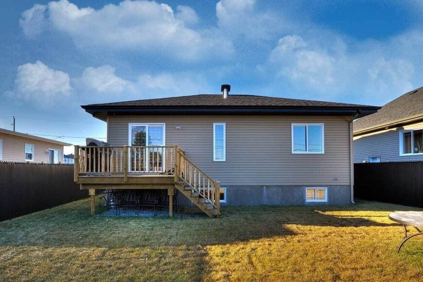 Rear view with taupe horizontal siding, glazed windows, and a wooden staircase that leads to the covered deck.
