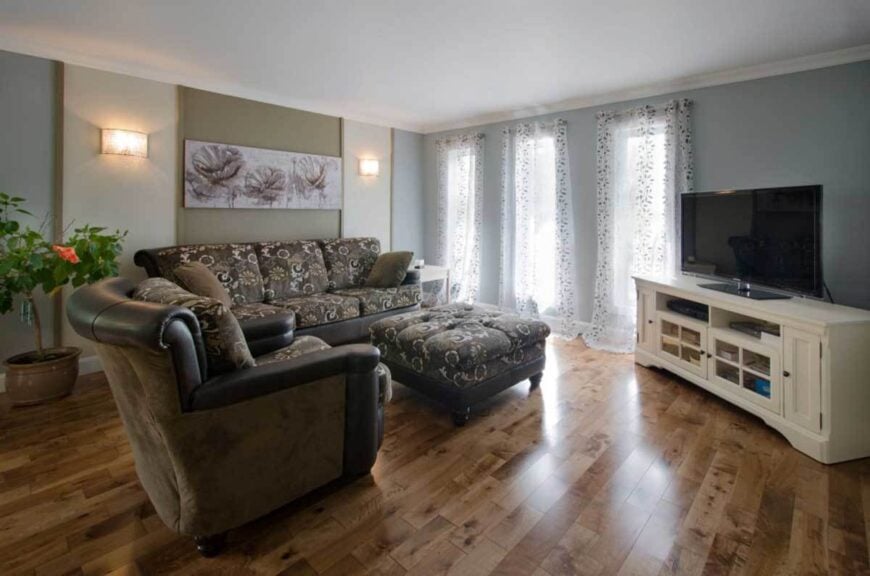 Living room with floral cushioned seats, a matching tufted ottoman, and a TV that sits on a white console table.