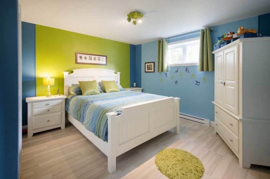 Kid's bedroom with multi-colored walls, white furnishings, and light hardwood flooring topped by a round shaggy rug.