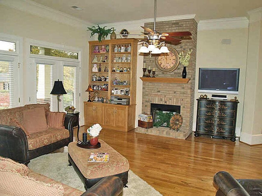 The living room offers cushioned seats, a matching ottoman, and a stone fireplace flanked by wooden cabinets.