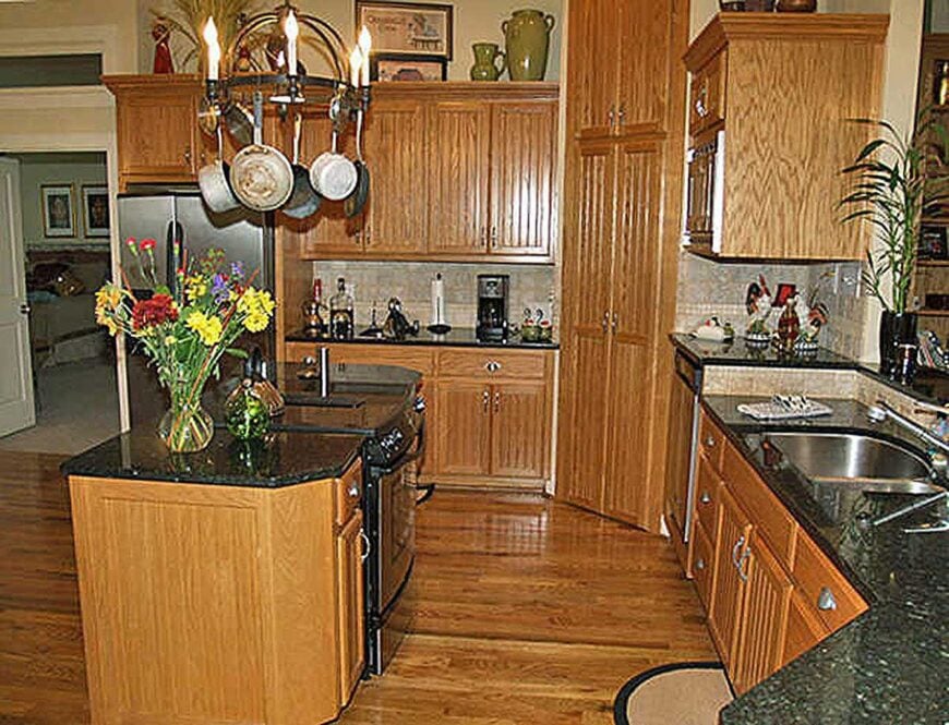 The kitchen is equipped with black granite countertops, an undermount sink, and hanging metal pot rack suspended over the center island.