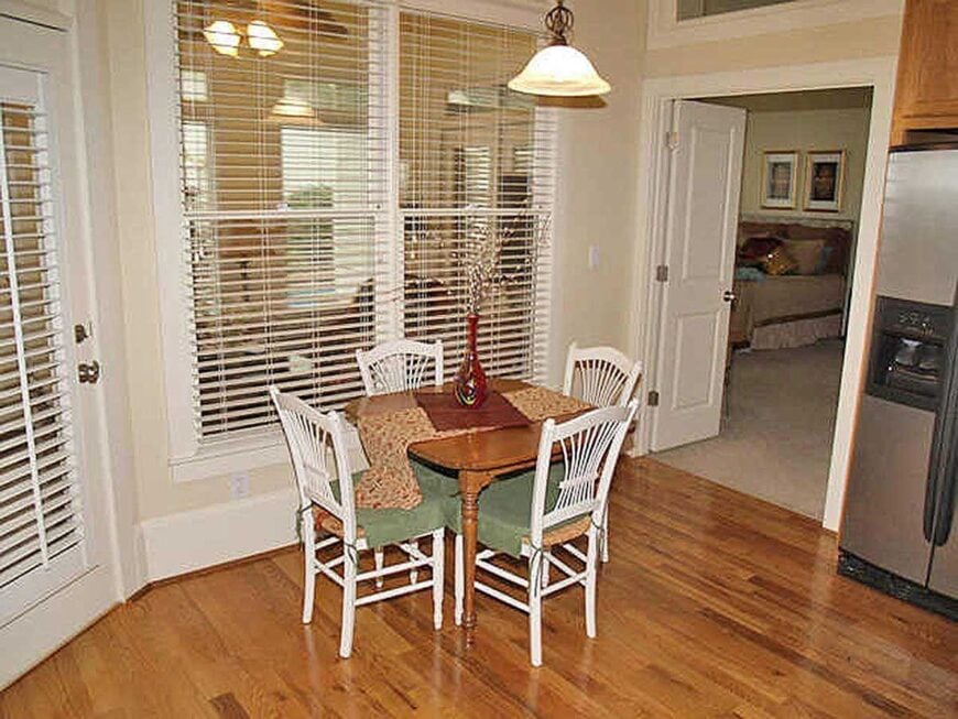 Breakfast nook with a glass dome pendant, white cushioned chairs, and a wooden table topped with a printed runner and a glass vase.