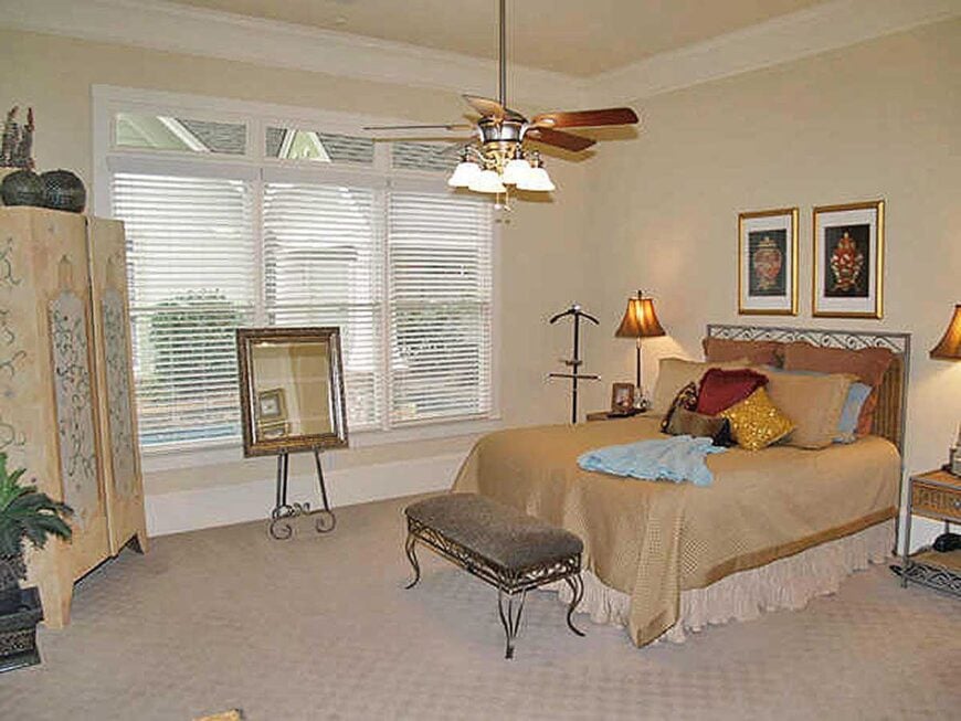 The primary bedroom is furnished with a cute wardrobe, matching nightstands, and a skirted bed complemented with a metal cushioned bench.