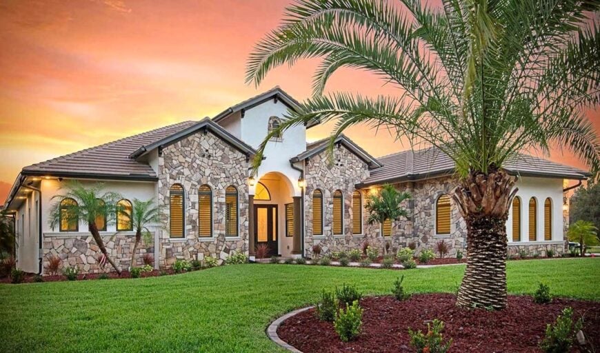 Lush plants and palm trees complement the home's facade embellished with captivating stone accents.