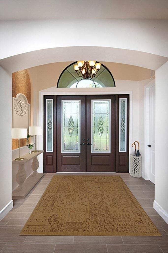 The foyer has a large vintage rug, a warm chandelier, and a light wood console table lit by sleek drum lampshades.