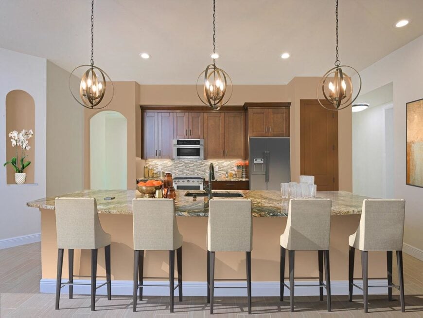 Spherical pendants along with recessed ceiling lights illuminate the kitchen with wooden cabinetry and a granite top island lined with beige counter chairs.