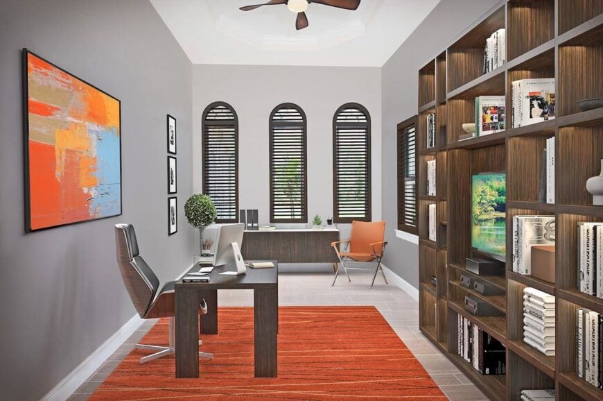 Striking orange hues from the armchair, bold painting, and area rug bring a pop of color on the gray home office.