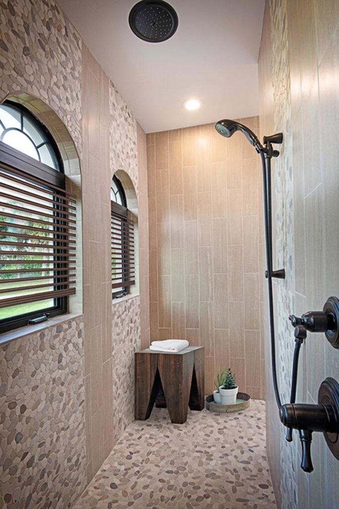 A closer look at the shower area shows the wrought iron fixtures, arched windows, and a wooden stool that doubles as a towel rack.