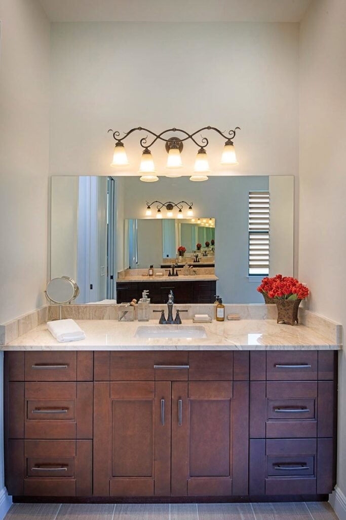 Frameless mirror lit by warm ornate sconces tops the sink vanity with an elegant granite countertop.
