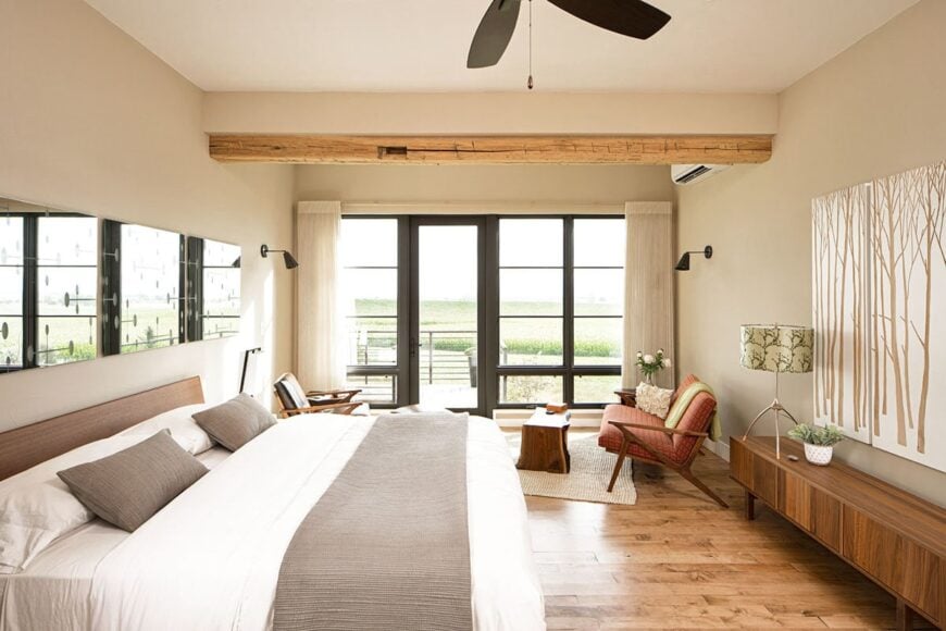 Primary bedroom with hardwood flooring, massive windows, and a regular ceiling lined with a rustic wood beam.