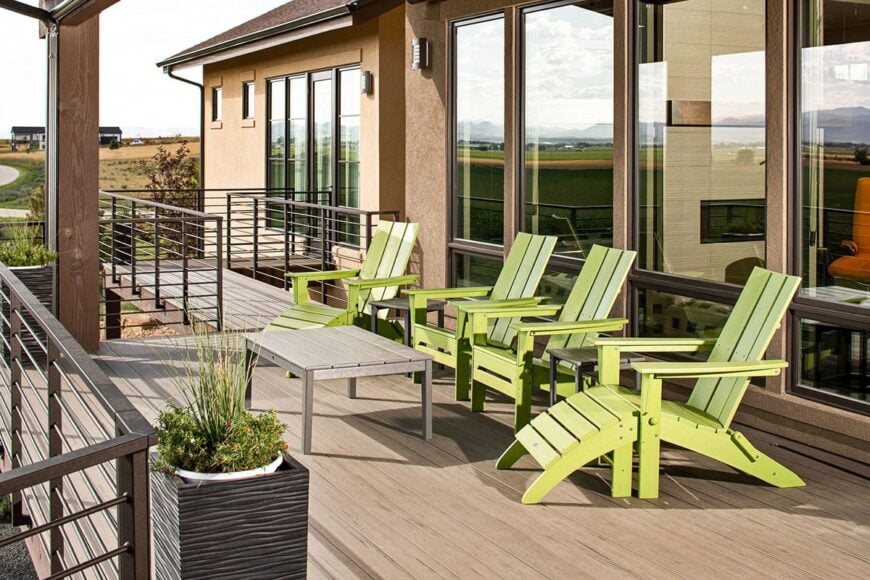 An expansive deck filled with green loungers, a wood plank table, and a potted plant.