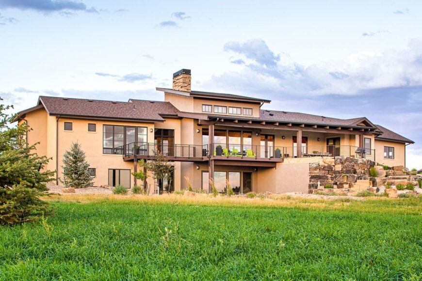 View of the house from the backyard showing the stucco exterior, clerestory windows, and a wide deck framed with wrought iron railings and wooden columns.