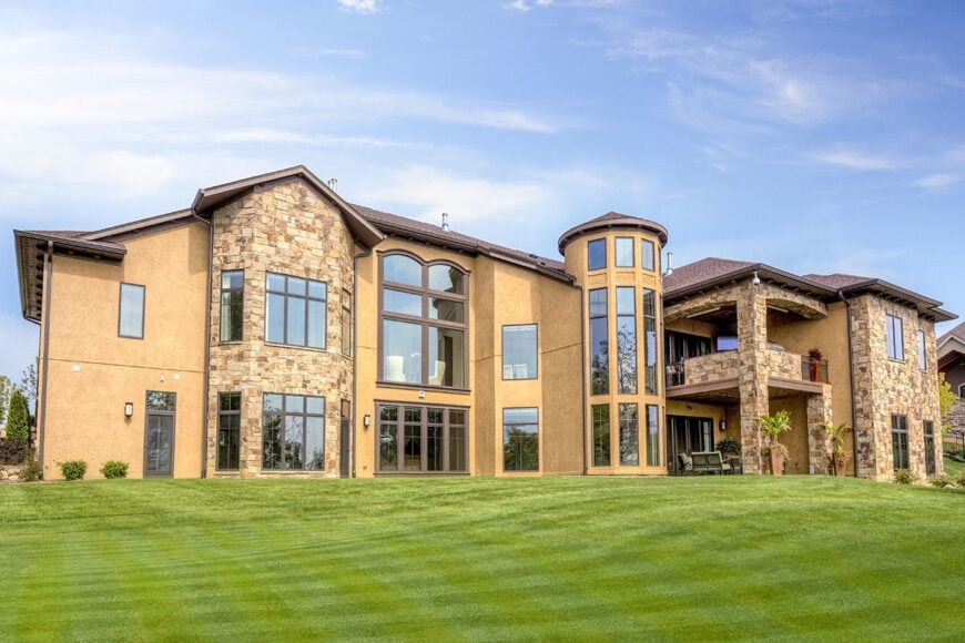 Home's rear view with a covered patio and balcony along with a tall turret filled with glazed windows.