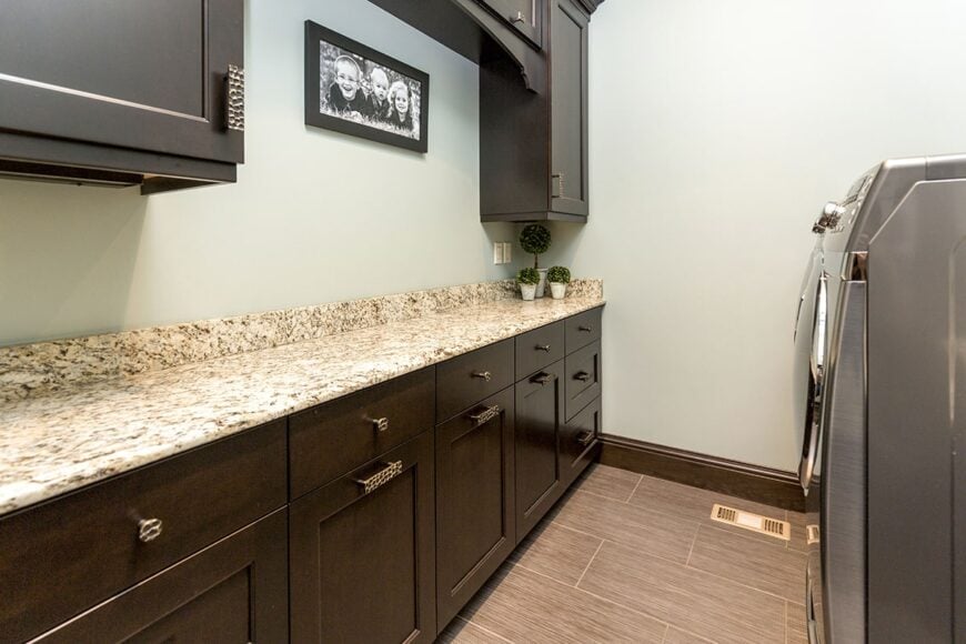 The utility room is equipped with front-load appliances, dark wood cabinets, and a granite countertop fixed against the light gray wall.