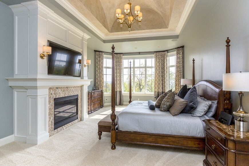 Primary bedroom with a barrel-vaulted ceiling, beige carpet flooring, and a bay window dressed in patterned draperies.