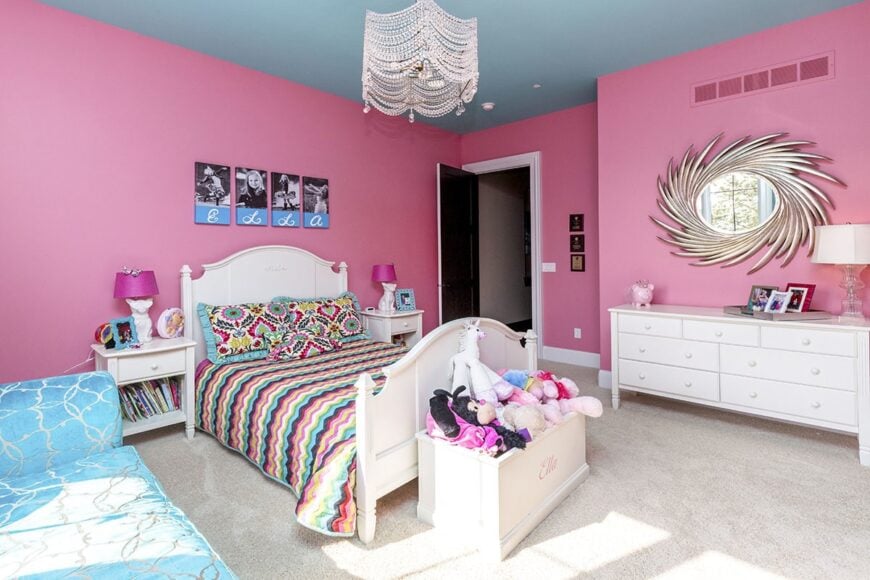 Kid's bedroom with blue regular ceiling and pink walls adorned with posters and a contemporary sun mirror.