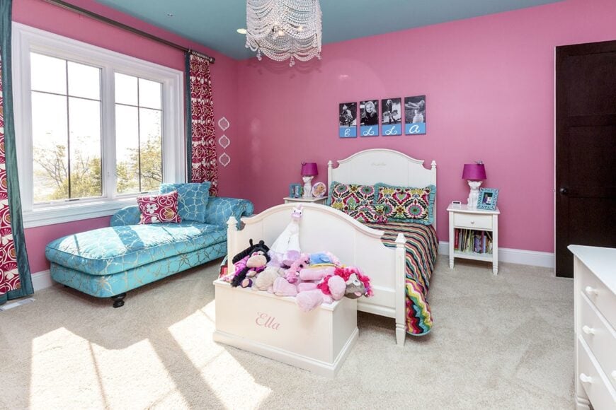The kid's bedroom is furnished with a blue chaise lounge, white dresser, and cute bed flanked by matching nightstands and magenta table lamps.