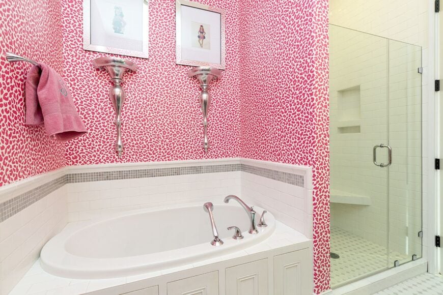 Kid's bathroom with a walk-in shower and a drop-in bathtub fixed against the pink patterned wallpaper.