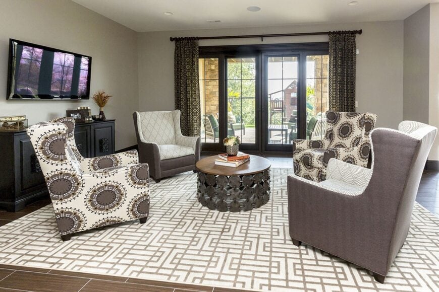 Recreation room with a wall-mounted TV, a black console table, and patterned wingback chairs surrounding the wooden round table over a beige area rug.