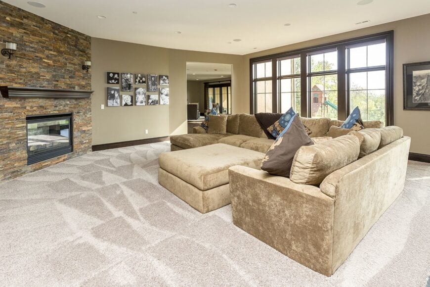 The family room has a velvet beige sofa, a matching ottoman, and a corner fireplace lined with a dark wood mantel.