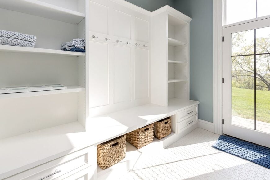 Mudroom with coat racks, white built-in shelves, and a bench seating with rattan baskets underneath.