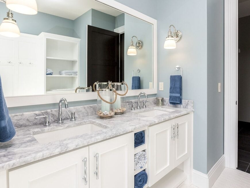 This powder room has a dual sink vanity and a large rectangular mirror mounted on the calming light blue wall.