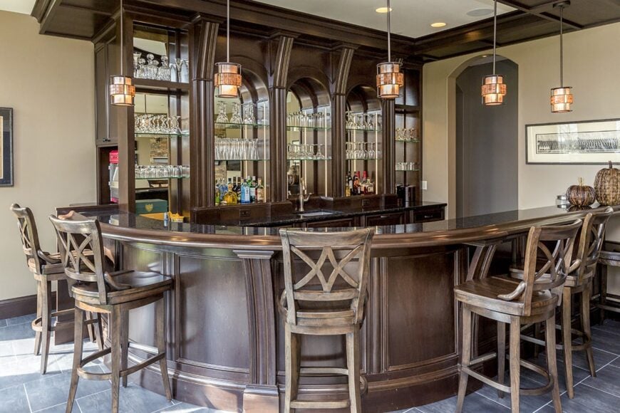 Glass and dark wood elements run throughout this wet bar. It is illuminated by warm glass pendants that hang over the curved peninsula.