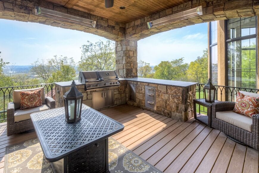 The covered porch is filled with a summer kitchen, wicker armchairs, and a perforated table sitting on a brown floral rug.
