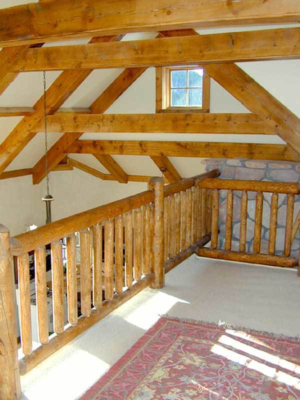 Open loft with wooden railings and beige carpet flooring topped by a floral area rug.