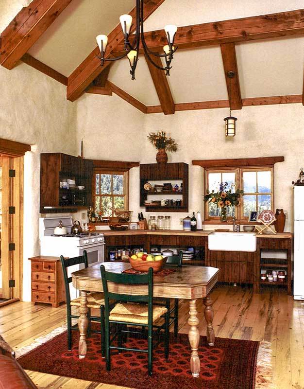 The eat-in kitchen is equipped with wooden and floating cabinets, a farmhouse sink, a white cooking range, and wooden dining set over a red patterned rug.