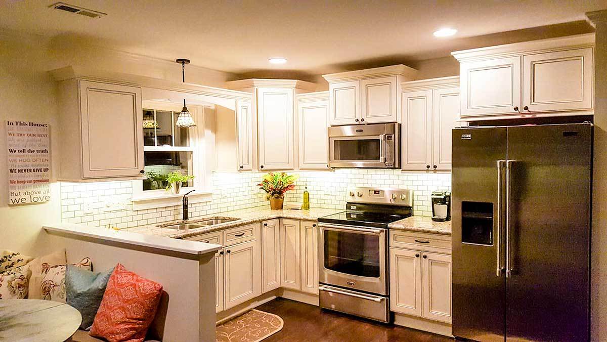 The kitchen is equipped with a double bowl sink, stainless steel appliances, white cabinets, and a peninsula that acts as a divider to the dining area.