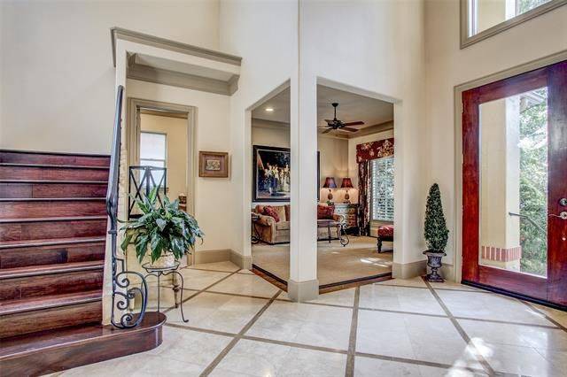 Spacious foyer with marble flooring and a wooden staircase that match the glass entry door.