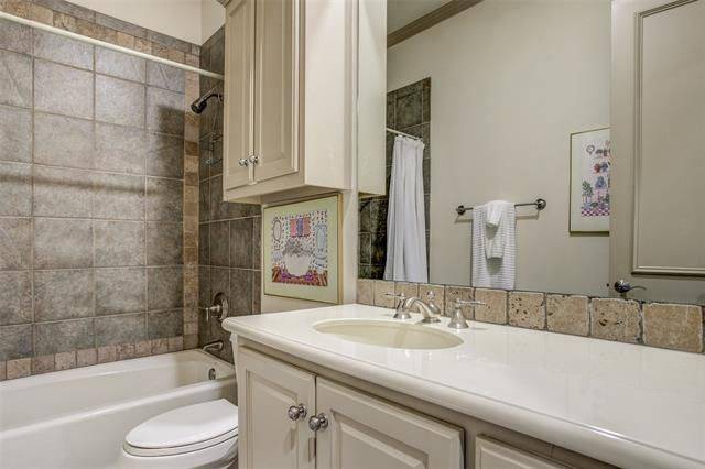Bathroom with a sink vanity, a toilet, and a tub and shower combo accentuated with brown tiled walls.