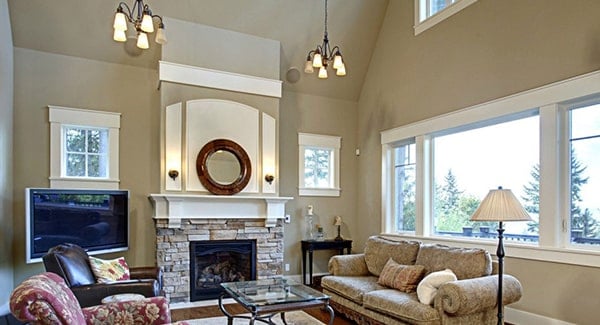 The living room has cozy seats, a glass top coffee table, warm chandeliers, and a stone fireplace with a round mirror on top.