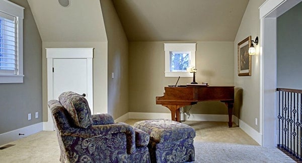 Second-floor loft filled with a baby grand piano and a floral lounge chair that's paired with a matching ottoman.