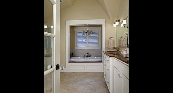 A glass door opens to the primary bathroom with large sink vanity and a deep soaking tub lit by a wrought iron chandelier.
