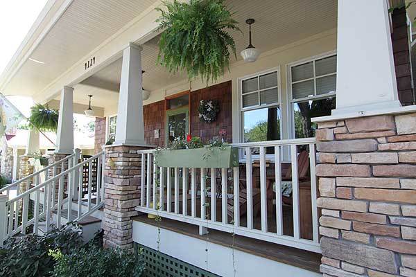 Stone columns and white wooden railings surround the front porch.
